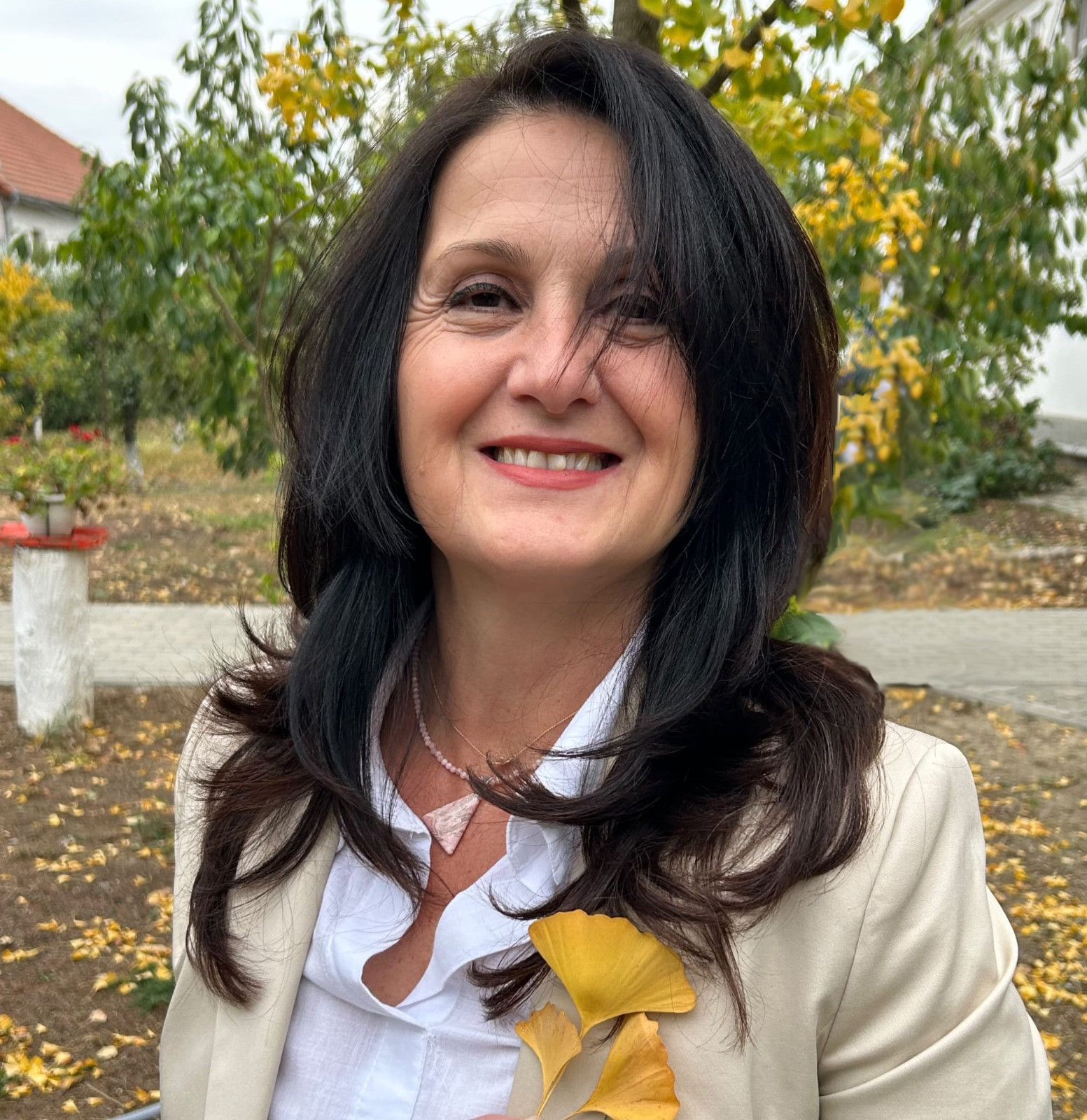 Portrait of Gabi smiling outdoors in a cream jacket with golden ginkgo leaves